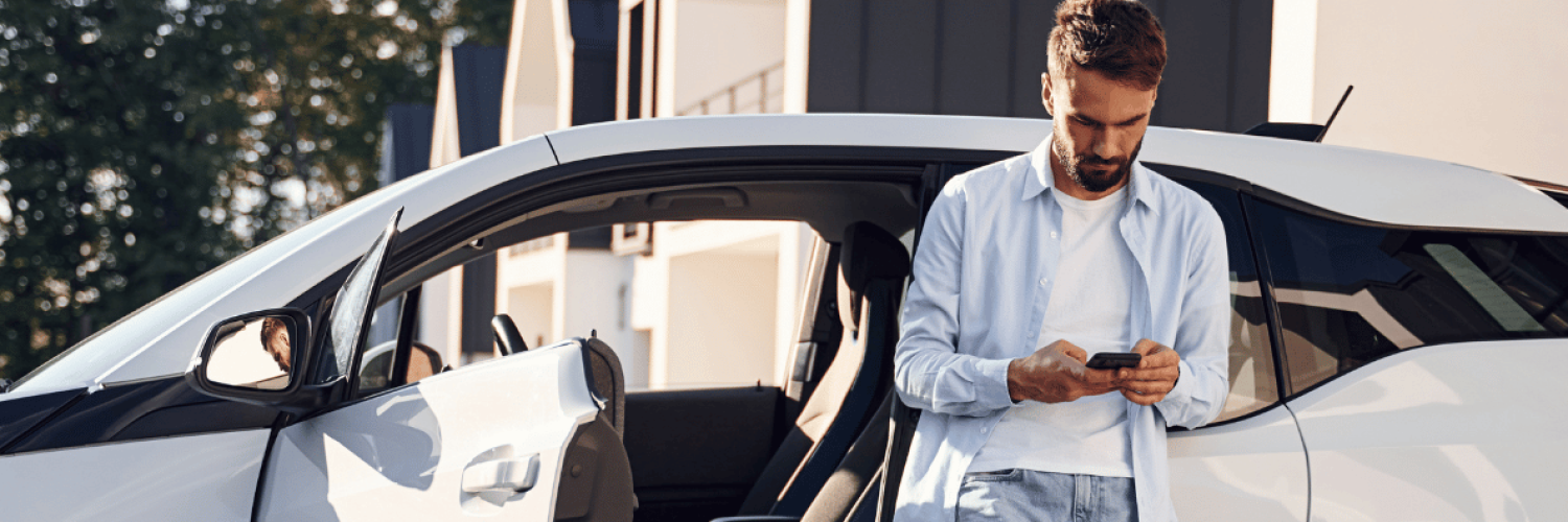 Man leaning up against car with phone in hand
