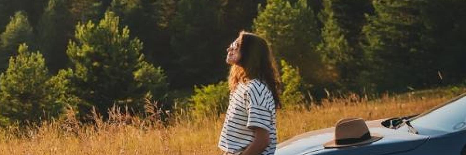 Kvinde læner sig op ad bil i naturen
